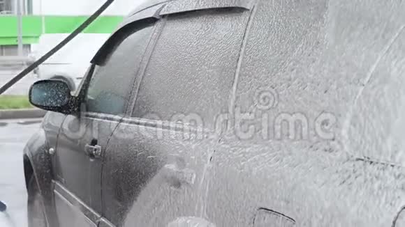 一个男人用肥皂泡沫清洗一辆黑色的汽车自助洗车过程慢动作视频视频的预览图