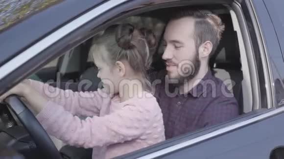 肖像小女孩坐在父亲的腿上在车上特写孩子正在学习开车微笑的男人视频的预览图