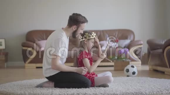 肖像年轻英俊的父亲把他可爱的长发女儿戴上皇冠她很高兴视频的预览图
