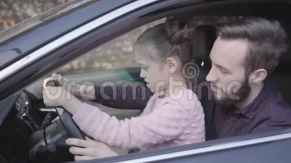 小女孩坐在爸爸身上她的腿在车里贴得很近孩子正在学习开车微笑男人花钱视频的预览图