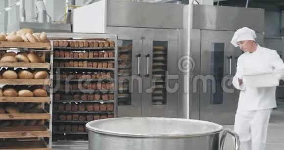 好看的老面包师准备面团加入面粉在工业容器背景工人移动和视频的预览图