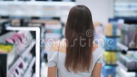 背面女孩在化妆品店购物在货架之间慢动作视频的预览图