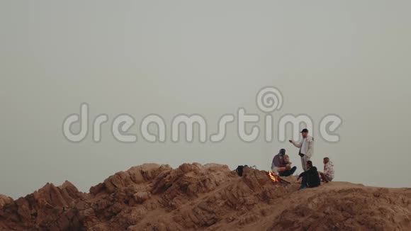 一群人在日落时分在山顶上放松坐在篝火旁享受他们的时光友谊青春视频的预览图