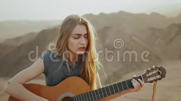女人在沙漠风景沙漠山脉背景慢动作全高清弹吉他和唱歌视频的预览图