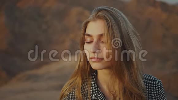 美丽的金发女人的肖像闭着眼睛看日落快乐的年轻女子站在沙漠中日落视频的预览图