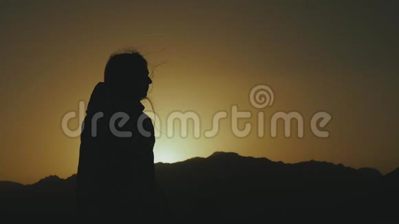 美丽的年轻女子在沙漠中日落时散步的剪影穿过沙漠沙丘风吹缓慢视频的预览图