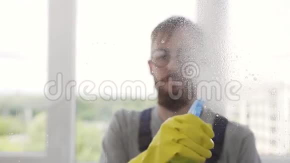 戴防护眼镜的长胡子清洁器在窗户上喷洒清洁剂视频的预览图