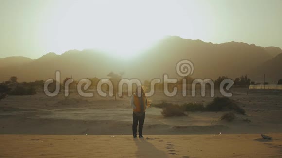 日落时漂亮女人的肖像快乐的年轻女子站在风中迎着沙漠中的日落美景慢动作视频的预览图