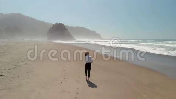 一位迷人的年轻女子在靠近林肯市的俄勒冈州海岸海滩散步的空中镜头视频的预览图