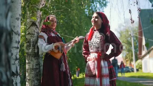 穿着俄罗斯民族服装的女人站在桦树附近其中一个扮演巴拉莱卡视频的预览图
