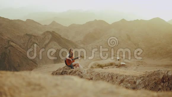 女人在沙漠风景沙漠山脉背景慢动作全高清弹吉他和唱歌视频的预览图