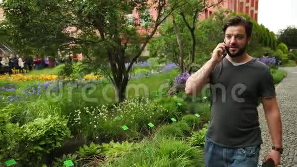 在花园里的花附近打电话的年轻人背景中的植物视频的预览图