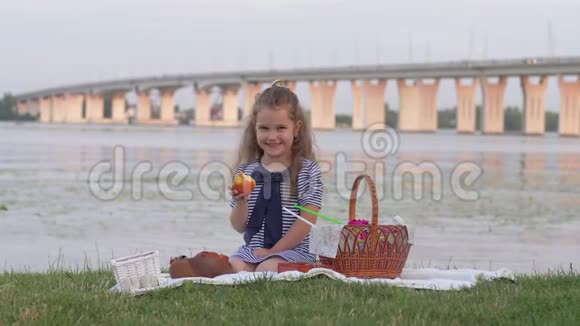小女孩微笑着在河边的大自然野餐时吃着新鲜的苹果放弃了拇指视频的预览图