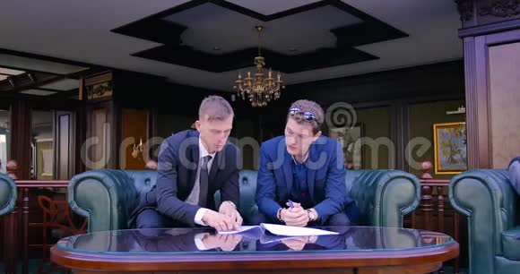 两个商人坐在漂亮的公寓里穿着西装讨论合同的签订合同的条款视频的预览图