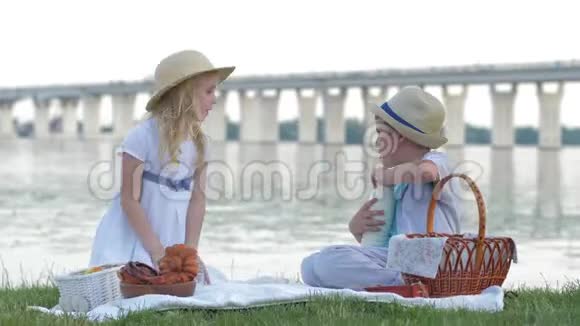 孩子们野餐小男孩把牛奶从瓶子里倒入玻璃杯里让女朋友在河边放松视频的预览图