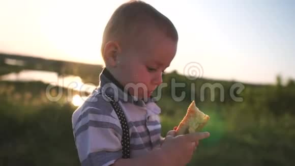 一个可爱的蹒跚学步的孩子在大自然的绿色植物中吃馅饼慢动作视频的预览图