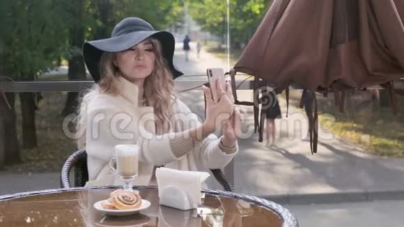 一位美丽的女士在户外咖啡馆里摆着智能手机自拍视频的预览图
