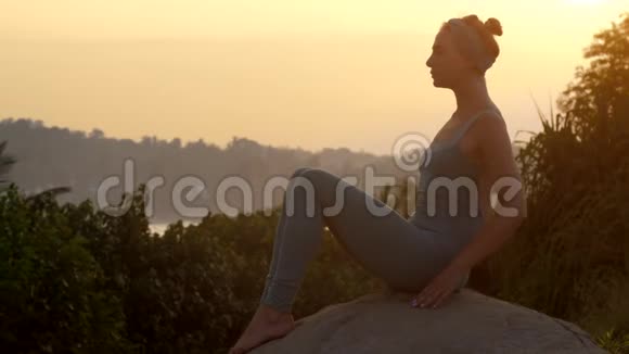穿着运动服的女孩做船上瑜伽摆在岩石上的慢动作视频的预览图