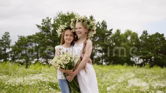 两个女朋友戴着花圈抱着花束在绿野上摆姿势年轻时尚模特摆姿势视频的预览图