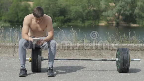 健身训练后坐着的年轻肌肉男用平板电脑视频的预览图