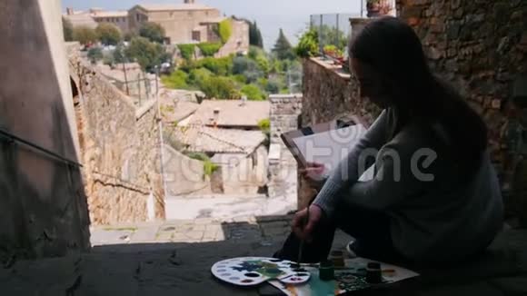 一个年轻的女人坐在楼梯上画风景背面视频的预览图