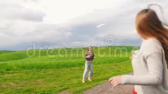两个笑的女人在绿色的田野上玩飞盘从后面看视频的预览图