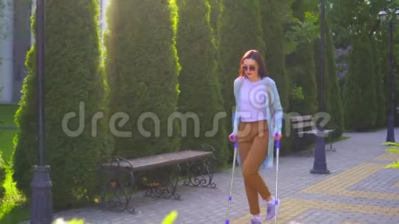 阳光城公园里一个身体受伤的漂亮年轻女子拄着拐杖走路视频的预览图