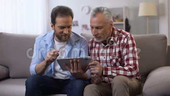 退休父亲和中年儿子滚动标签看着和微笑的相机视频的预览图