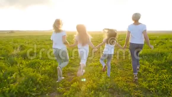 友谊的概念年轻快乐的女人和她们的女儿在日落时分跑过田野视频的预览图