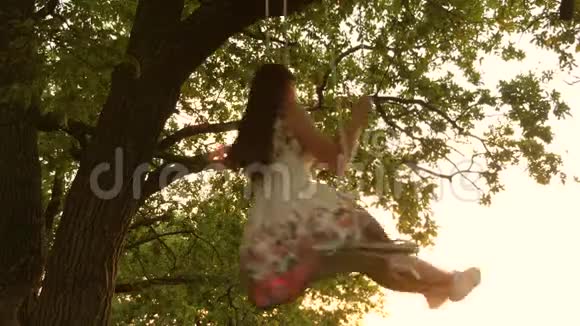 飞行的梦想快乐的童年概念年轻女孩在橡木树枝上的绳索秋千上摆动一个漂亮的女孩视频的预览图