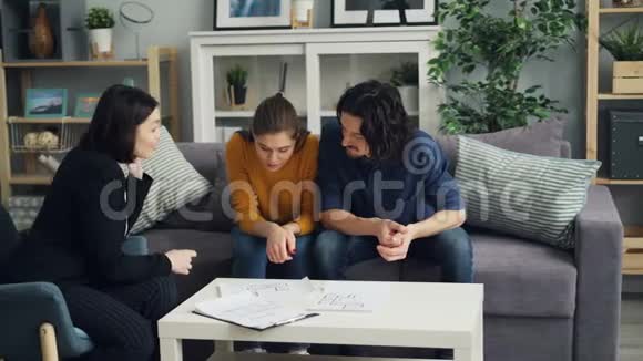 一对年轻夫妇在新房子里和房地产经纪人在室内看报纸视频的预览图