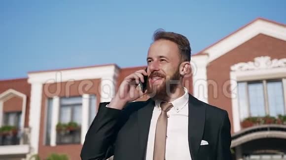 在豪华的房子附近一个长着大牙的长着好看微笑胡须的男人在打电话视频的预览图