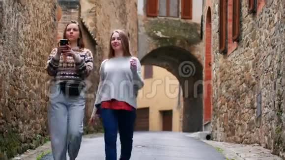 两个年轻的女人沿着一条狭窄的街道走着说话其中一人拍照视频的预览图