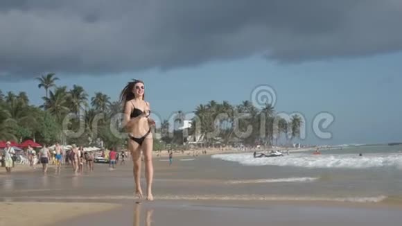 美丽的运动女孩在斯丽兰卡海滩上长发欢乐沿着岸边在水上奔跑视频的预览图