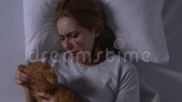 受伤的女士抱着泰迪熊在床上哭泣受害者需要支持视频的预览图