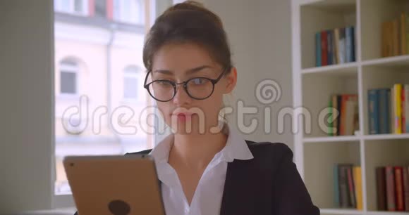 一位年轻漂亮的白种人女商人戴着眼镜在平板电脑上看着镜头微笑的特写镜头视频的预览图
