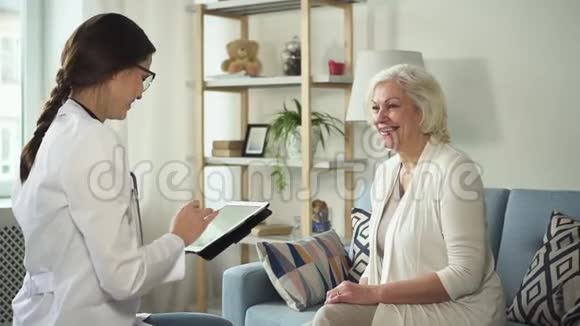 年轻护士使用平板电脑拜访健康的退休妇女视频的预览图