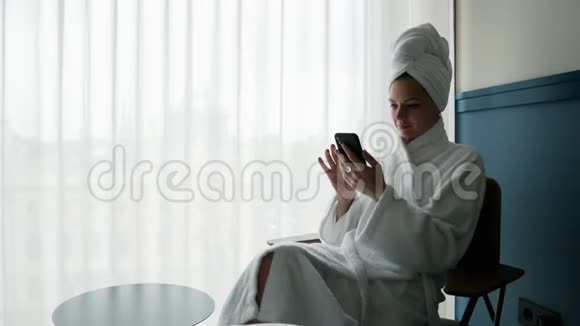 穿着浴袍头上戴毛巾的美女肖像使用手机视频的预览图