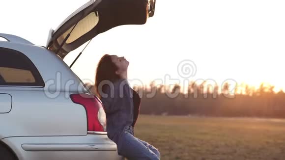 在黄金时光的最后几分钟美丽的年轻女子在欧洲的一次公路旅行中汽车后备箱里快乐地跳舞视频的预览图