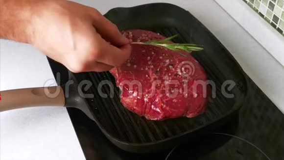 男人用手把一枝迷迭香放在加盐和胡椒的牛肉牛排上视频的预览图