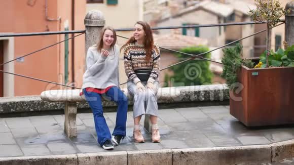 两个年轻的女人坐在长凳上其中一个向另一个人展示视频的预览图