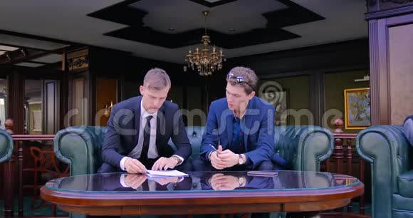 两个商人坐在漂亮的公寓里穿着西装讨论合同的签订合同的条款视频的预览图