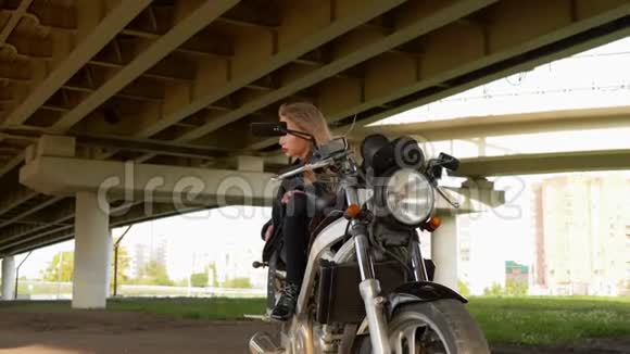 漂亮的女孩穿着莫托衣服坐在黑色摩托车上穿着皮夹克骑摩托车的年轻骑自行车女孩视频的预览图