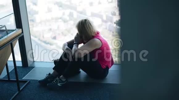 那个女孩坐在摩天大楼一扇明亮的大窗户前的地板上视频的预览图