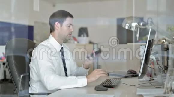 愤怒的中年商人用手机和办公室电脑说话视频的预览图
