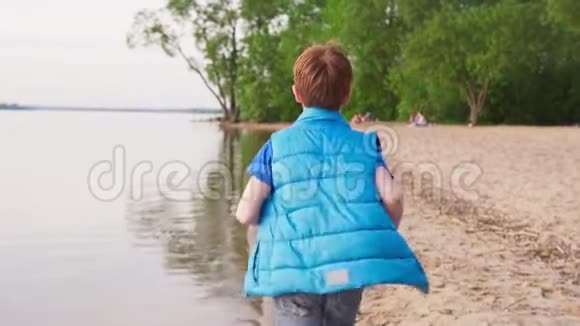 男孩在沙滩上奔跑沿着夏日的海岸线视频的预览图