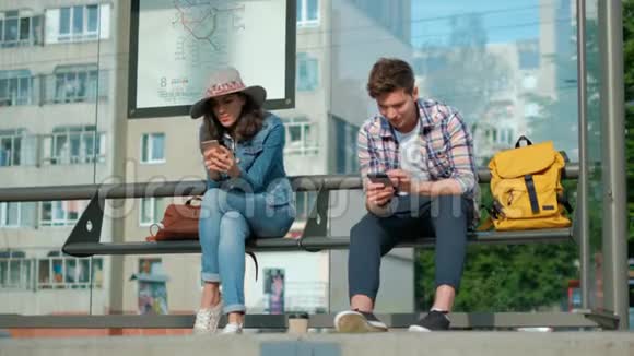 男人和女人坐在一起在运输站他们拿着现代的小玩意用互联网娱乐视频的预览图