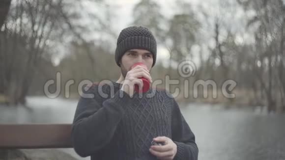 春天公园里坐在河边的长凳上喝红茶或咖啡的帅哥的画像视频的预览图