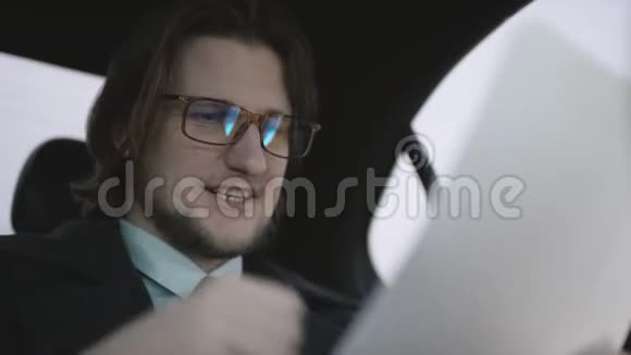 漂亮的男人棕色头发穿着开心果衬衫灰色外套骑着车用钢笔检查文件视频的预览图