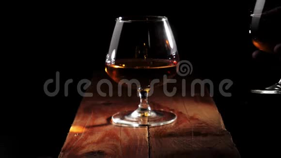 豪华白兰地黑色背景的棕色木桌上有金色干邑的玻璃手再放一杯白兰地视频的预览图